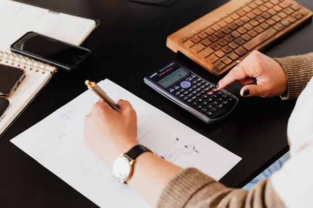 Home crop woman using calculator and taking notes on paper
